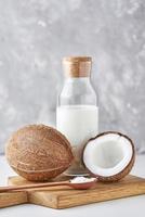 Coconut milk in glass bottle and fresh coconuts with half on a gray background photo
