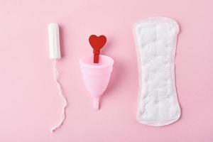 Sanitary pad, menstrual cup, tampon and red wooden heart on a pink background photo