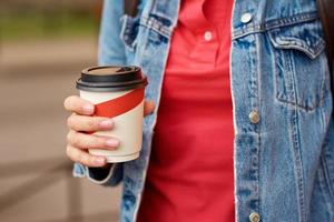 Woman hand with paper cup of coffee take away in a city street photo
