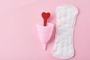 Sanitary pad, menstrual cup and red wooden heart on a pink background photo