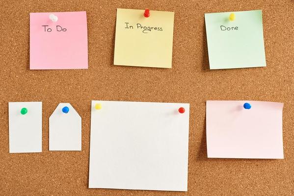Colorful paper notes with words To do, In progress and Done pinned on a cork board