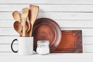 Kitchen utensils in cup and brown plate on white photo