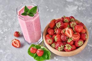 Strawberry smoothie in glass jar and fresh strawberries in wooden bowl photo