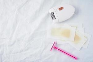 Epilator, razor and wax strips on white background photo