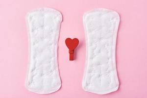 Two sanitary pads and red wooden heart on a pink background photo