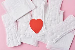 Sanitary pads with red heart on a pink background, top view photo