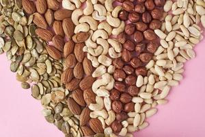 Different types of nuts and pumpkin seeds on a pink background, top view photo