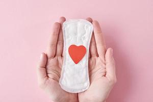 Woman hands hold sanitary pad with red heart on a pink background photo