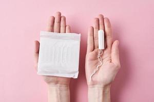 Woman hands hold sanitary pad and tampon on a pink background photo