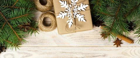 Christmas background with gift boxes wrapped in kraft paper, fir tree branches, pine cones, cinnamon and star anise on white wooden background. Flat lay, top view photo