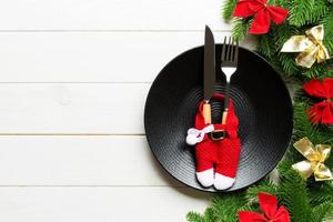 Holiday composition of plate and flatware decorated with Santa clothes on wooden background. Top view of Christmas decorations. Festive time concept photo