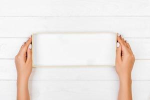 Woman hands holding empty white box on gray background. View from above photo