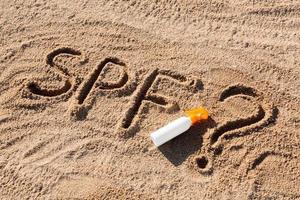 Sun protect factor. SPF word written on the sand and white bottle with suntan cream with question mark. Skin care concept background photo