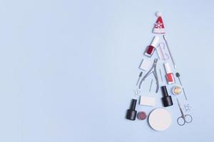 Manicure tools and nail polishes are laid out in the shape of a Christmas tree with copy space on blue background photo