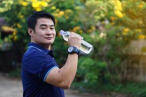 Handsome Asian man traveler holds bottle of drinking water to drink outdoors. Concept ,Drinking water for health, Healthy lifestyle.Quenching thirst, reduce fatigue, refreshes body. photo