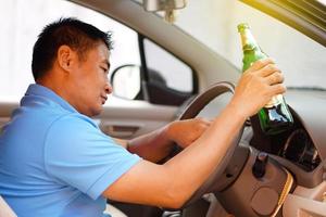 un borracho asiático sostiene una botella de cerveza para beber en el auto. concepto, deja de conducir mientras bebes alcohol o campaña de whisky. ilegal y peligroso conducir un vehículo que conduce a un accidente. foto