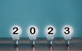 Turn On shine bright light bulb with 2023 Happy New Year on the desk and copy space for text decoration. photo