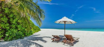 Beautiful tropical sunny shore, couple sun beds chairs umbrella under palm tree leaves. Sea sand sky. Romantic relax lifestyle panoramic island beach background. Summer travel exotic vacation panorama