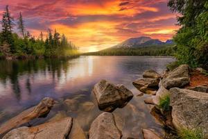 Awesome nature landscape. Beautiful scene with high Tatra mountain peaks, stones in mountain lake, calm lake water, reflection, colorful sunset sky. Amazing nature background. Autumn adventure hiking