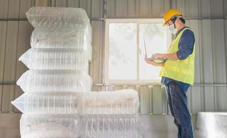 Young man worker and quality inspector in a factory checking number of white plastic bottles in the warehouse photo