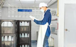 Young man worker or quality inspector in workwear and with a protective mask on his face working in checking bottled drinking water in drink water factory before shipment.drinking water business photo