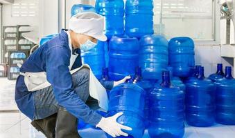 Inspection quality control. man worker in workwear and with a protective mask on his face working in a drink water factory checking water gallons before shipment. photo