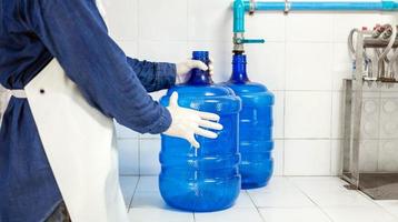 hombre trabajador en ropa de trabajo y con una máscara protectora en la cara trabajando produce agua potable en una fábrica de agua potable limpia. línea de producción de agua potable limpia foto