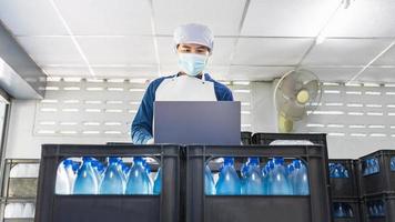 Young man worker or quality inspector in workwear and with a protective mask on his face working in checking bottled drinking water in drink water factory before shipment.drinking water business photo