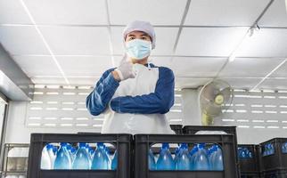 trabajador joven o inspector de calidad en ropa de trabajo y con una máscara protectora en la cara trabajando en el control de agua potable embotellada en la fábrica de agua potable antes del envío.negocio de agua potable foto