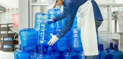 Inspection quality control. man worker in workwear and with a protective mask on his face working in a drink water factory checking water gallons before shipment. photo