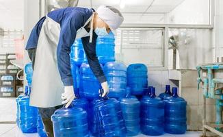 Inspection quality control. man worker in workwear and with a protective mask on his face working in a drink water factory checking water gallons before shipment. photo