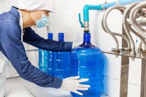 hombre trabajador en ropa de trabajo y con una máscara protectora en la cara trabajando produce agua potable en una fábrica de agua potable limpia. línea de producción de agua potable limpia foto