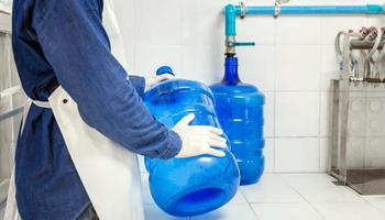 hombre trabajador en ropa de trabajo y con una máscara protectora en la cara trabajando produce agua potable en una fábrica de agua potable limpia. línea de producción de agua potable limpia foto