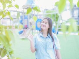 Portrait of an Asian woman with black hair and blue shirt wearing jeans and leaves. with a public garden background photo