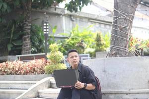 Attractive young Asian man using laptop confused in co-working space with unhappy face photo