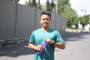 joven asiático calentándose para correr por la mañana y beber agua mineral foto