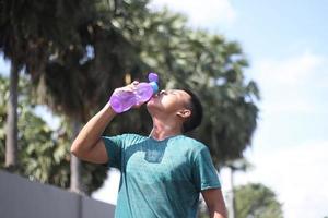Young asian boy warming up for jogging in the morning and drinking mineral water photo