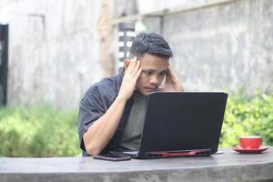 Un joven asiático atractivo que usa una laptop confundido en un espacio de trabajo conjunto con una cara infeliz foto