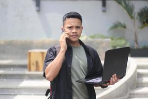 Attractive young Asian man using laptop in co-working space with happy face and calling her friend photo