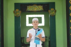 Young asian muslim praying in the mosque carrying a prayer mat photo