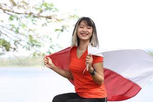 beautiful young asian woman carrying the indonesian flag with a cheerful face photo