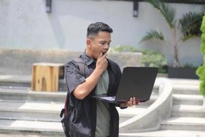 Attractive young Asian man using laptop confused in co-working space with unhappy face photo