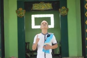 Young asian muslim praying in the mosque carrying a prayer mat photo