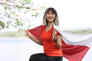 bella joven asiática que lleva la bandera indonesia con una cara alegre foto