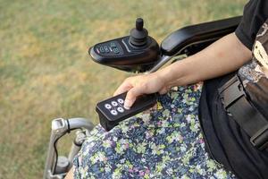 mujer asiática paciente en silla de ruedas eléctrica con joystick y control remoto en la sala del hospital de enfermería, concepto médico fuerte y saludable foto