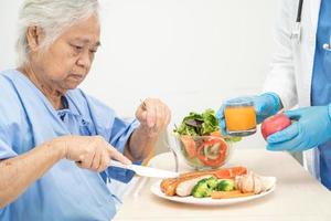 paciente asiática mayor o anciana anciana desayunando y comiendo vegetales saludables con esperanza y feliz mientras está sentada y hambrienta en la cama en el hospital. foto