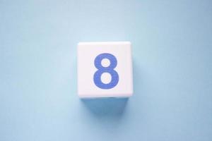 Close-up photo of a white plastic cube with a blue number 8 on a blue background. Object in the center of the photo