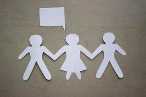 Silhouette of two man and woman between them, holding hands, cut out of white paper. With speech-bubble. In the center of the photo on a beige background.