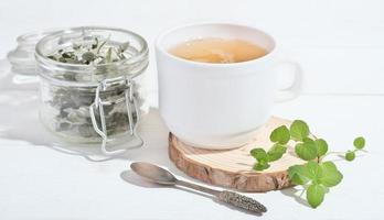 té verde de hierbas en taza blanca con hojas frescas y secas de menta y frambuesa. té de hierbas naturales para un desayuno saludable foto