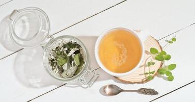 green herbal tea in white mug with fresh and dry leaves of mint and raspberry. natural herbal tea for healthy breakfast. top view photo
